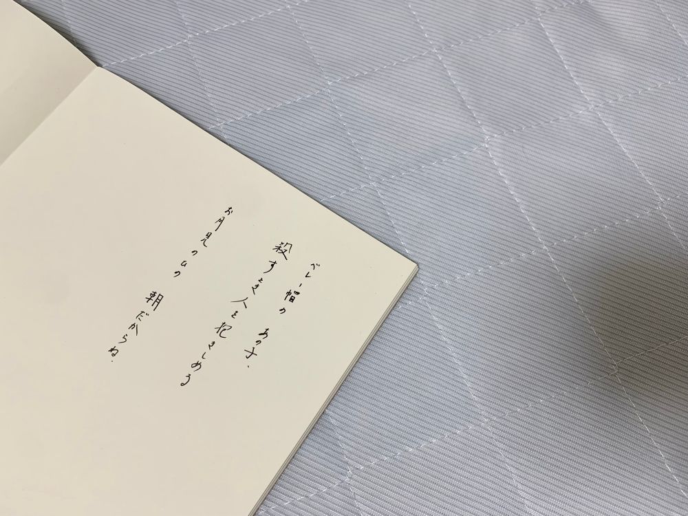 無地のノートの写真です。ベレー帽のあの子、殺すとき人を抱きしめる。お月見の日の、朝だからね」という自由詩が書いてあります。