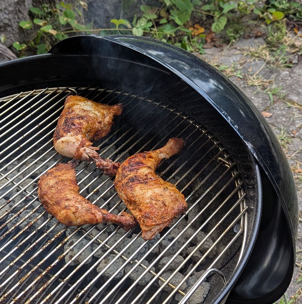Three chicken leg quarters finishing up on a charcoal grill.