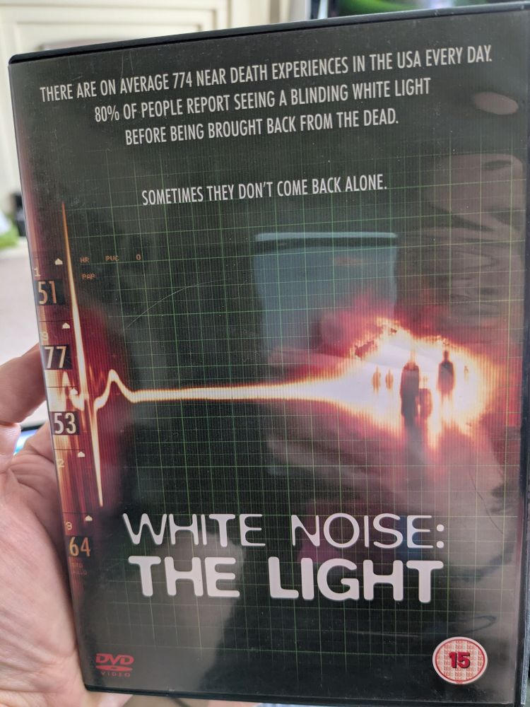 DVD for White Noise 2: The Light, rated 15. Depicts a heart monitor flatlining, but the line turns into a burst of light filled with the shadows of the dead.
Tagline: "There are on average 774 near death experiences in the USA every day. 80% of people report seeing a blinding white light before being brought back from the dead. Sometimes they don't come back alone."