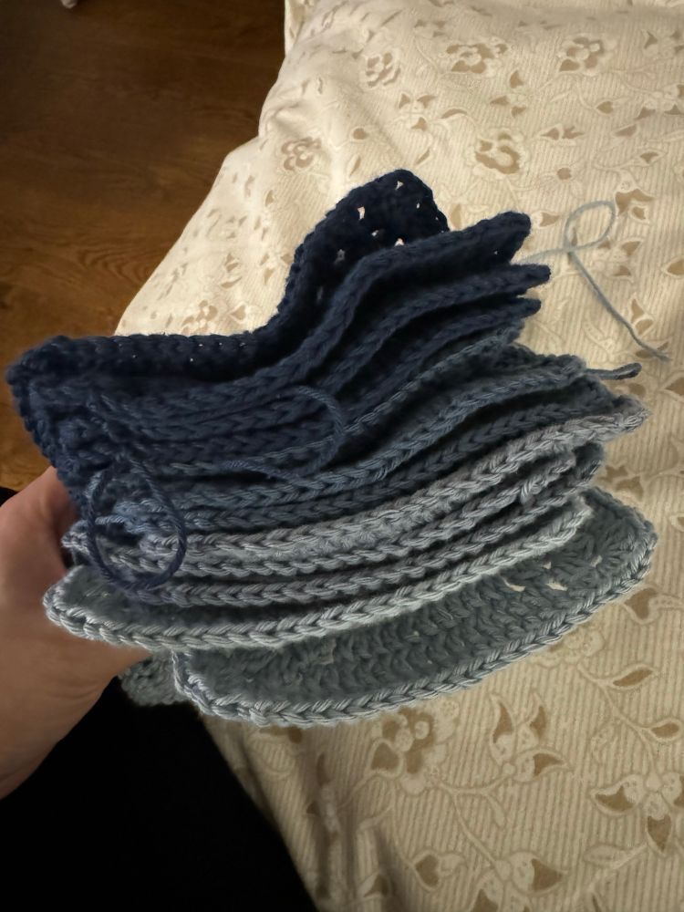 A stack of crochet granny squares in four different blue hues, shown from the side.