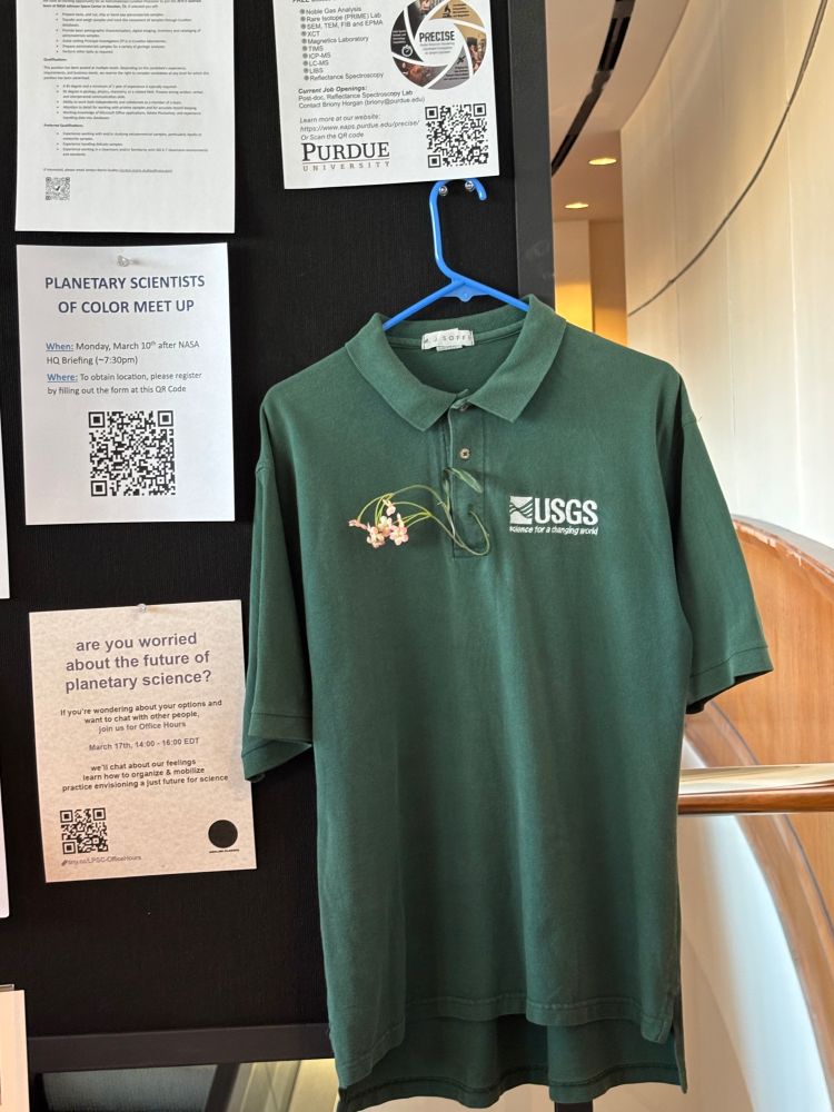 A green polo with the USGS logo is being hung up. A string of flowers is woven in the button holes. The shirt is hung up on the bulletin board. 