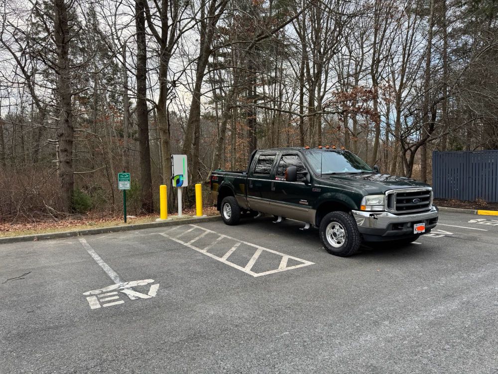Older Ford pick up truck parked in an EV charging station parking spot. 