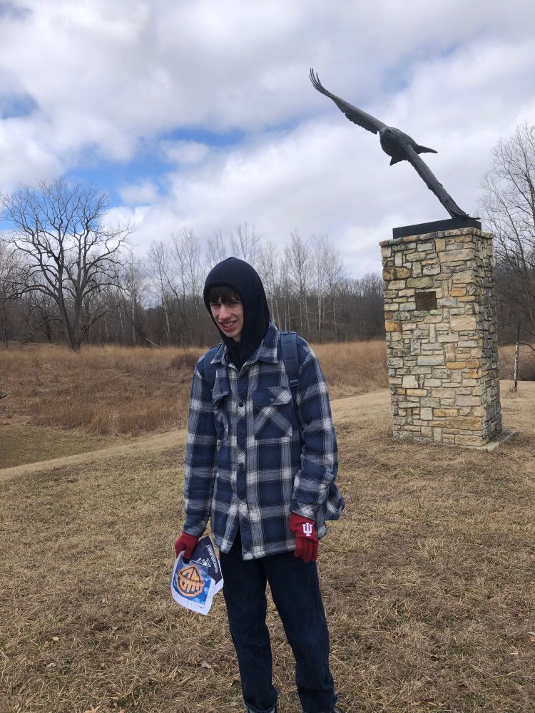 Tall boy in front of stone pillar with huge bronze eagle in flight above his head.