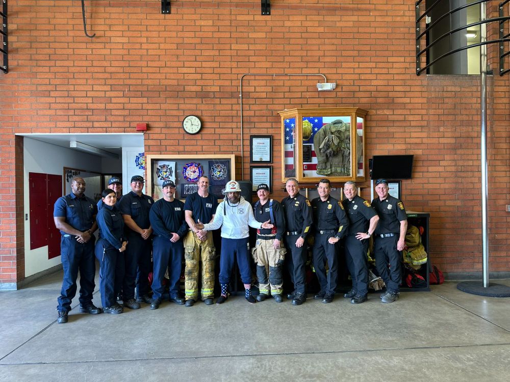 Mr. T wearing slippers and American flag socks standing next to firefighters.