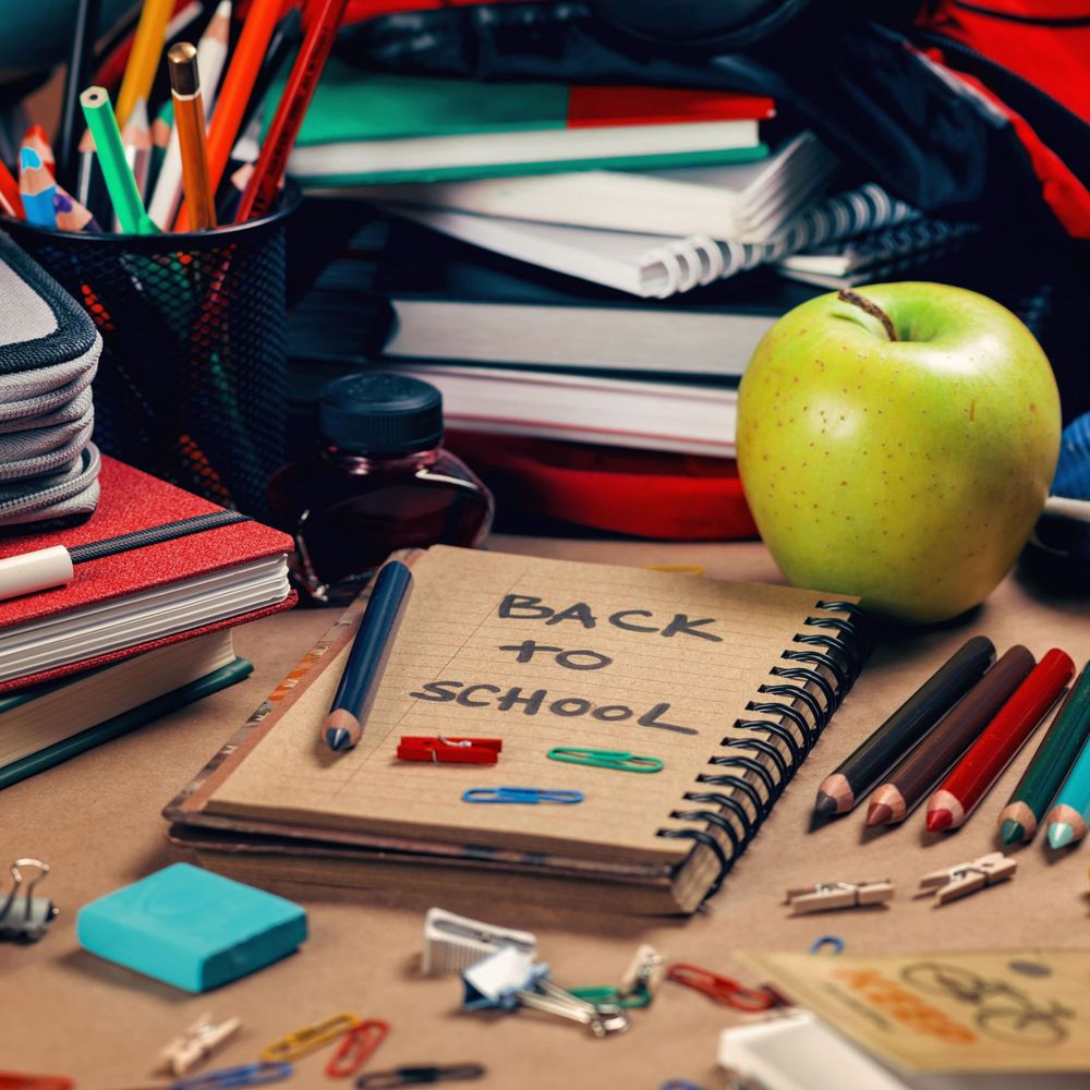 Desk with notebooks, colored pencils, pens, an eraser, paper clips, an apple, and a notepad labeled "Back to School."