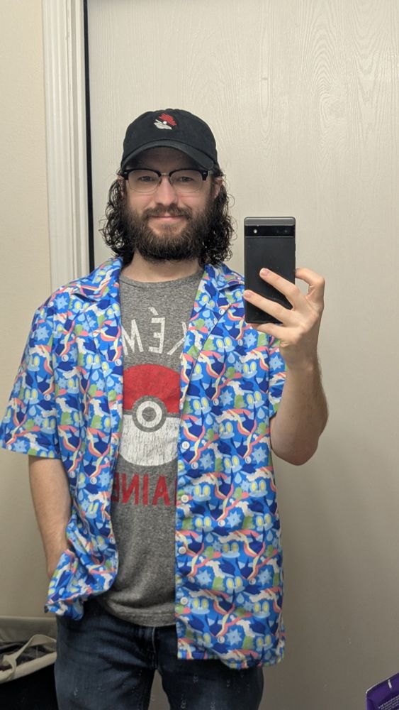 Justin in the mirror wearing a Pokéball hat, Greninja pattern button-up, Pokémon trainer Tshirt, and jeans