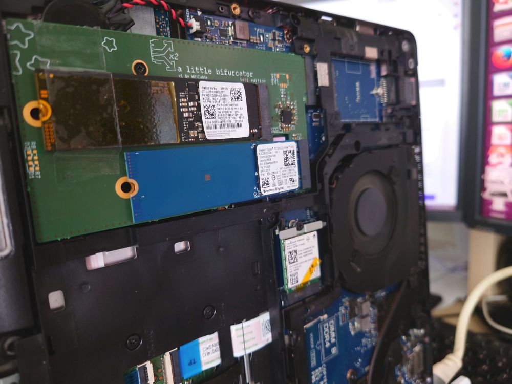 A picture of a Dell Latitude 5491 laptop with the bottom cover removed, showing a custom PCB installed in the SSD slot which is in turn host to 2 SSDs, filling up the otherwise unused empty space in the laptop.