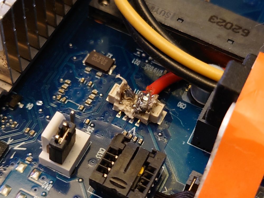 A red 5V wire soldered to the pins of a connector on the motherboard, plastic housing completely molten