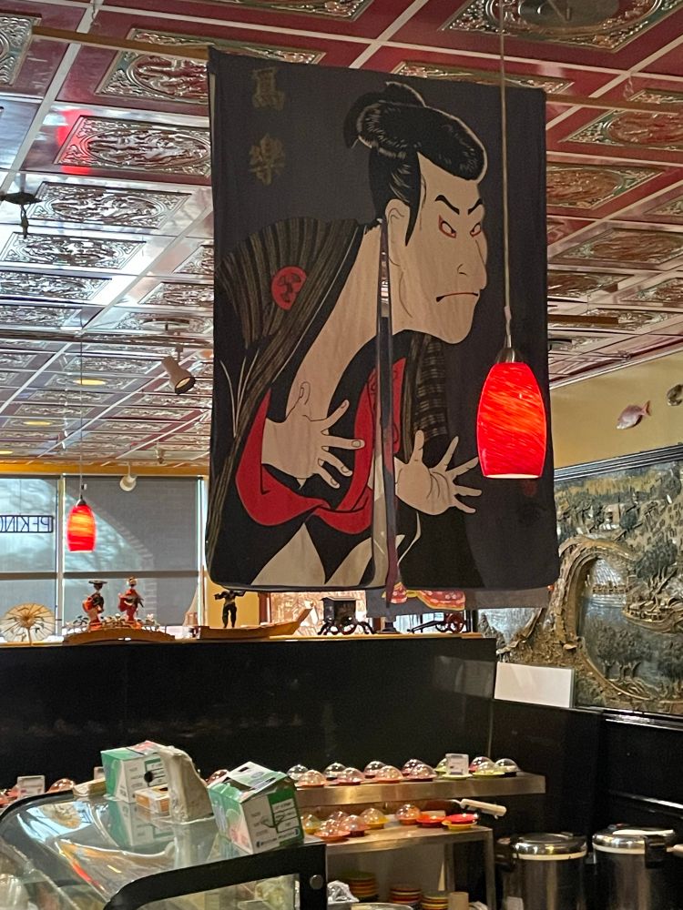 Reproduction of a famous wood block print of a kabuki character hanging over a sushi bar.