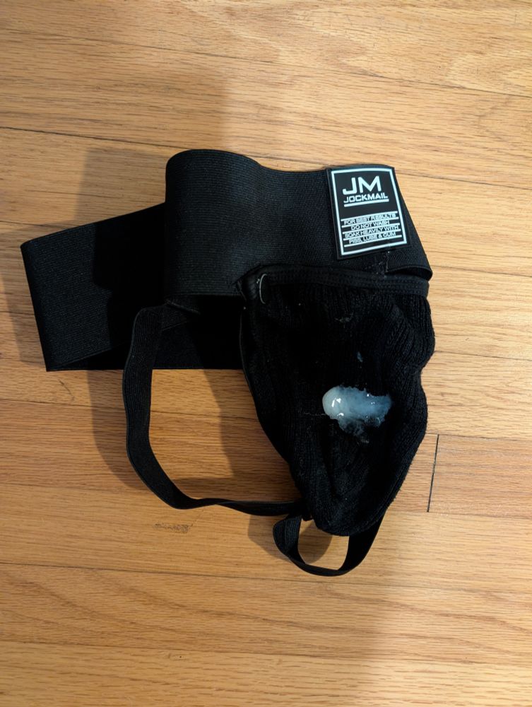 A black jockstrap lying on the floor, with a curiously pale stain near the crotch.