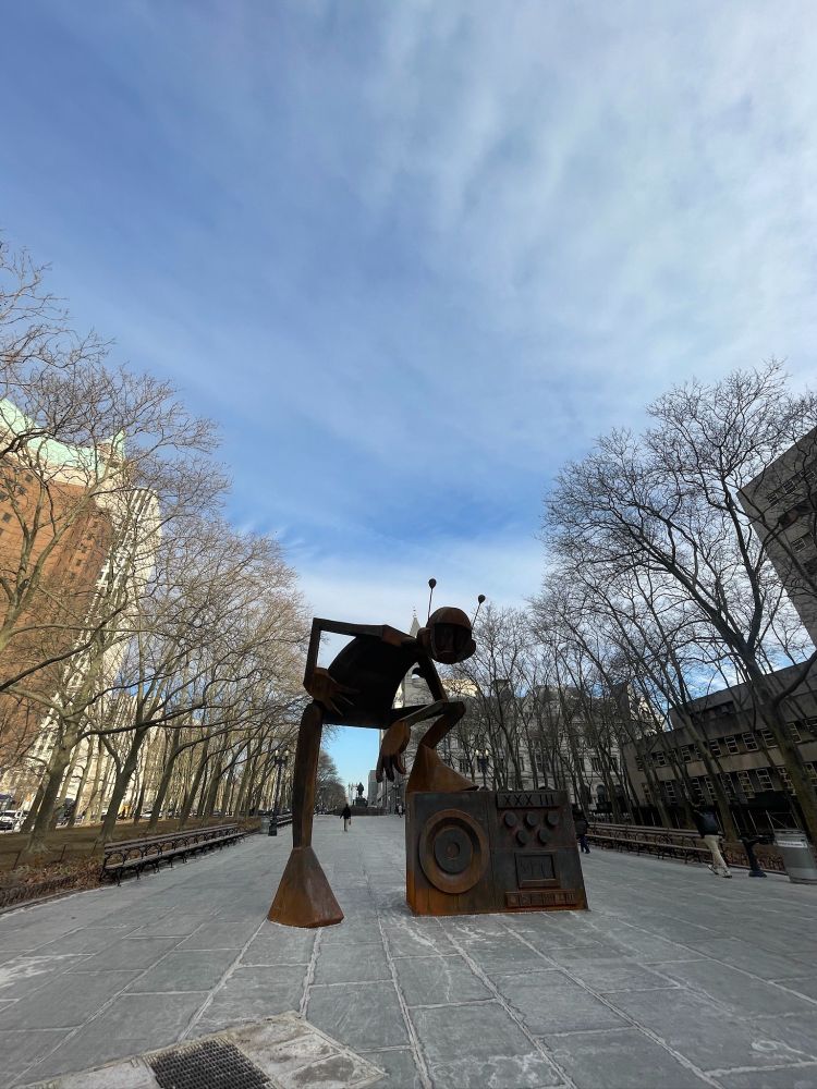 A large sculpture of a person with a background of blue sky and trees.