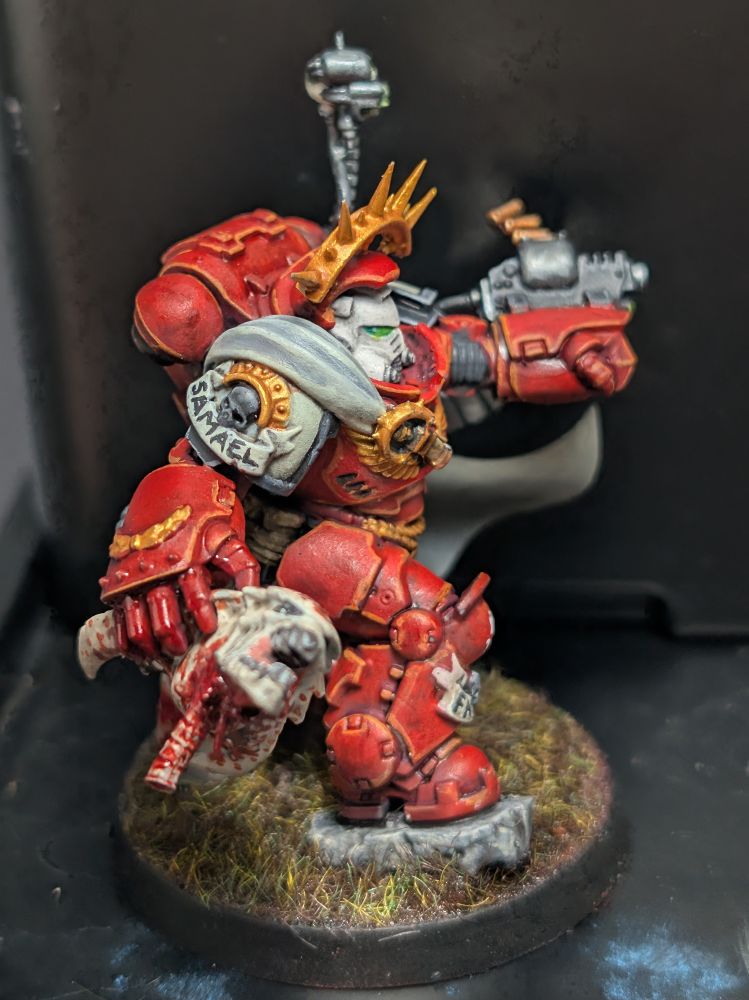 Captain in grav armor painted in Blood Ravens colors, holding a tyranid warrior head. Photo from the right.