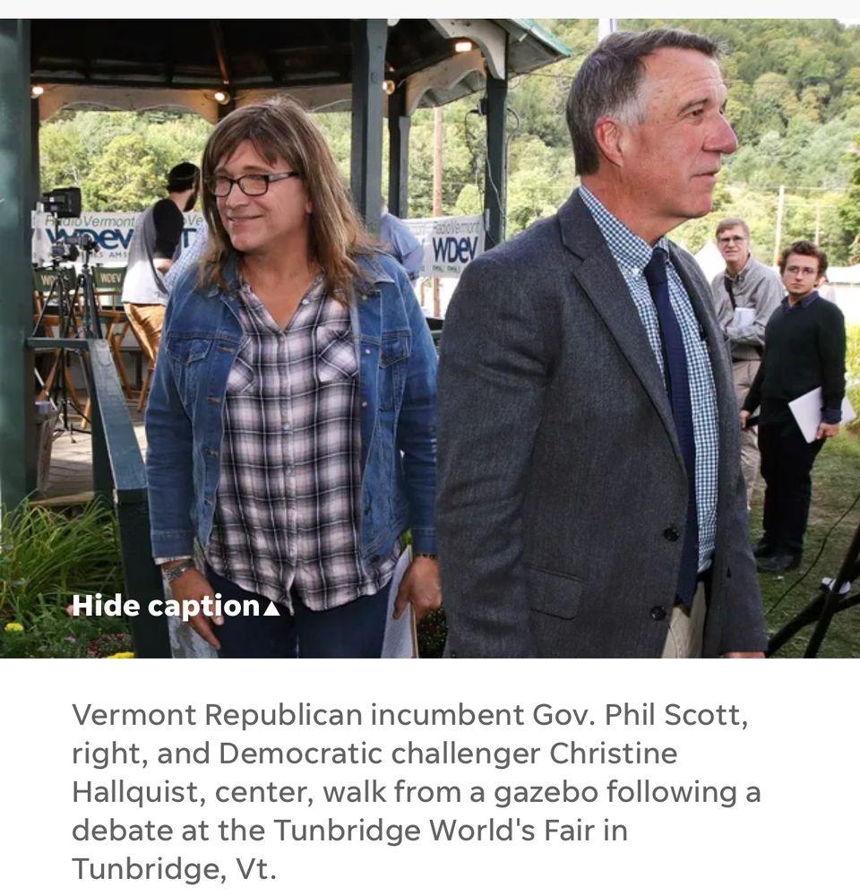 A man and a woman walk away from a gazebo with two onlookers. The man is wearing a jacket and tie with a tastefully plaid shirt. The woman is wearing a plaid button down and a jeans jacket. The caption reads “Vermont Republican incumbent Governor Phil Scott, right, and Democratic challenger Christine Hallquist, center, walk from a gazebo following a debate at the Tunbridge World’s Fair in Tunbridge Vermont”