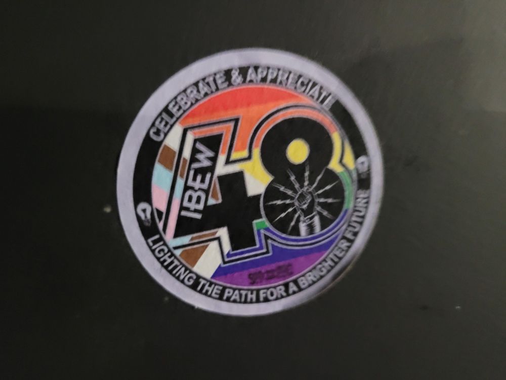 A round sticker for the international brotherhood of electrical workers union with a white border followed by a black ring with text that says 