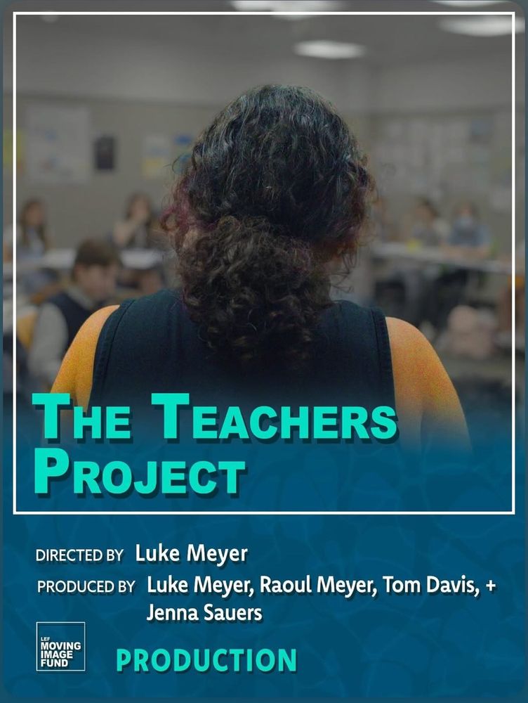 Image Description: Seen from behind, a figure with long curly dark hair looks ahead into an out-of-focus classroom where students sit.