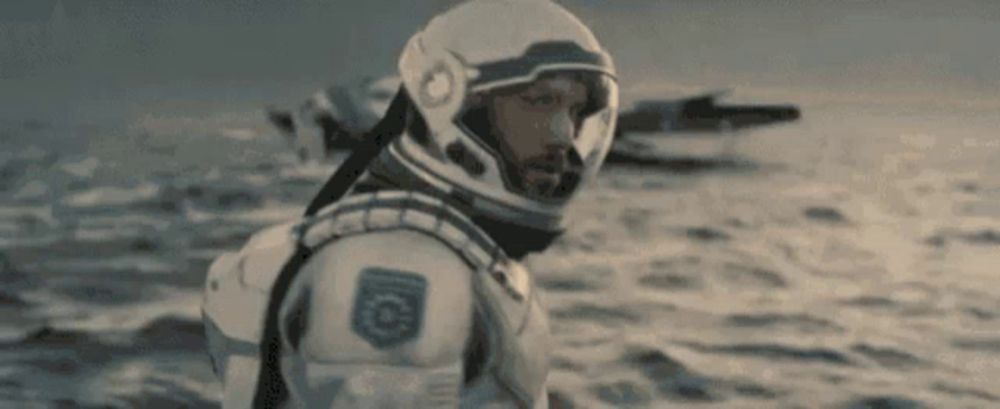 a man in a space suit and helmet is standing in the ocean .