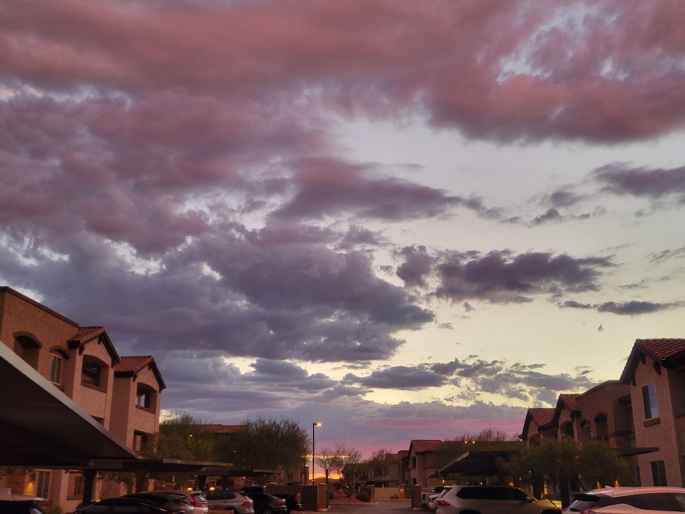 A fading sunset reflecting off clouds, with apartment building and car parking on both sides of the bottom of the frame 
