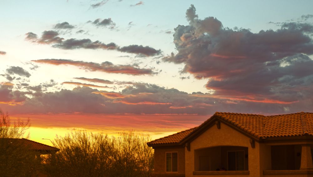 A bright yellow and red sunset reflecting off clouds behind an apartment building in the Southern Arizona sky