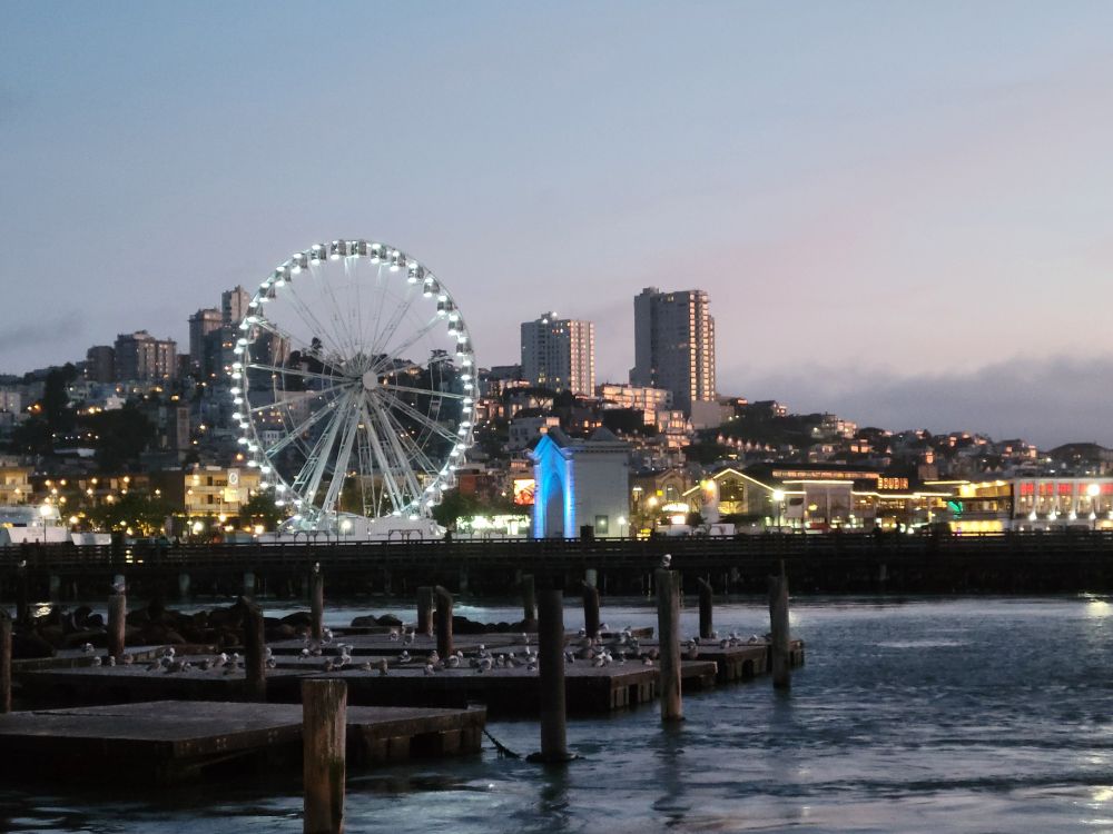 A sunset view of the ferris wheel and background city buildings near Pier 39 near San Francisco, California