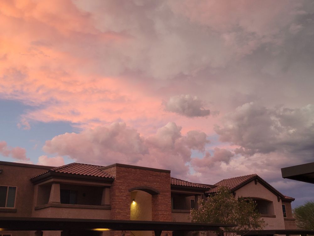 A pink and red sunset reflecting off clouds behind some apartment buildings in the Southern Arizona sky