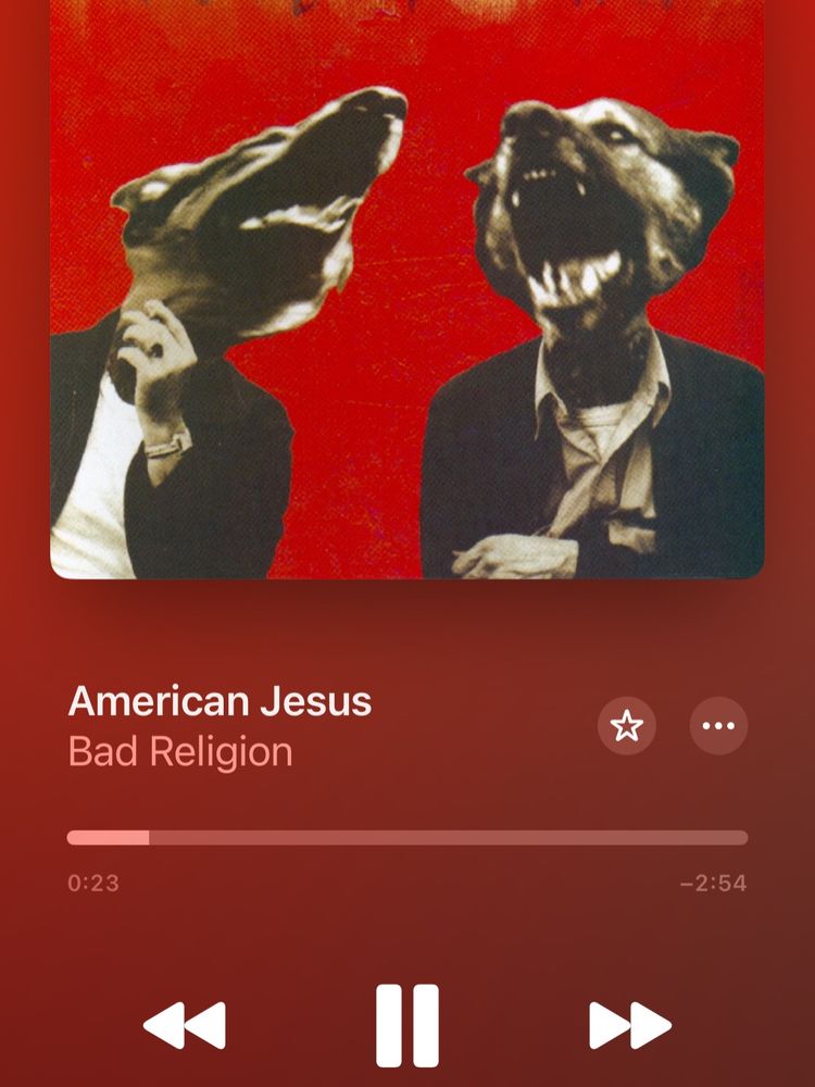 Image of cover art for the Bad Religion song "American Jesus," depicting two men in suits, but the heads are German Shepards instead of human heads. This is on a plain red background.