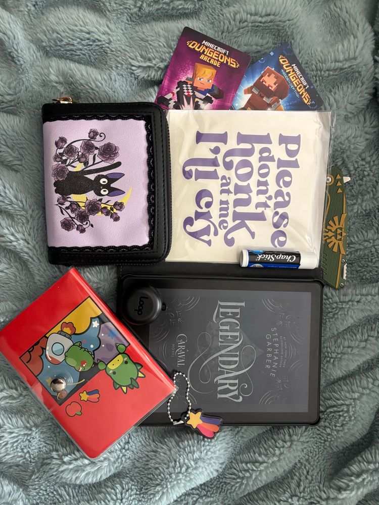 A picture of everything in my bag including my kindle, Kiki wallet, Dino notebook, Zelda *accessory and a car sticker that says please don’t honk at me I’ll cry 