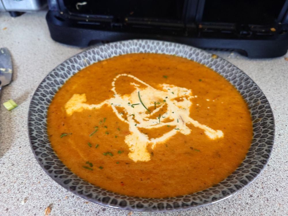 A bright orange soup in a bowl, it has some cream in the middle of it. Mmmm soup