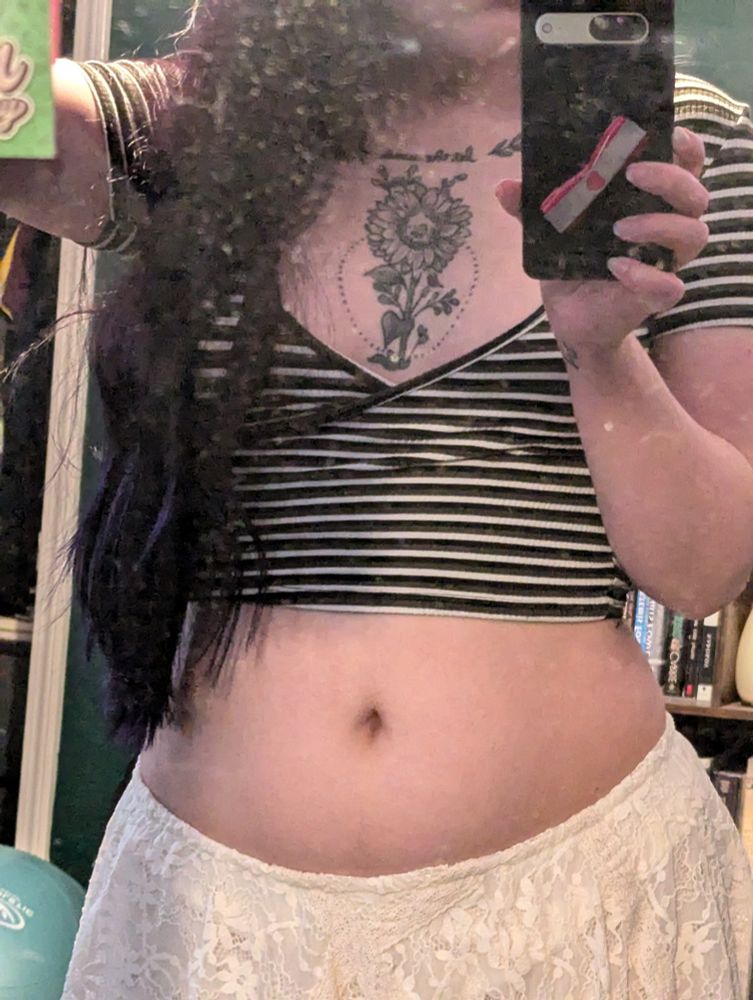 mirror selfie wearing a very deep cut striped crop top and a lace skirt