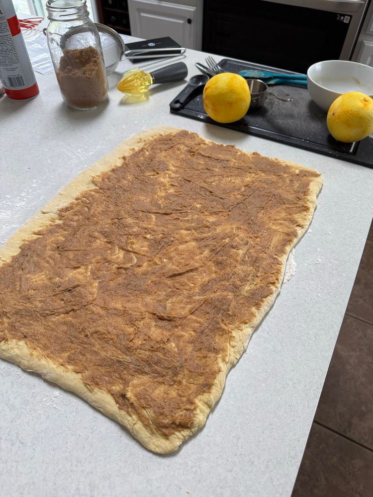 A sheet of dough with filling spread on top, partway thru making orange rolls