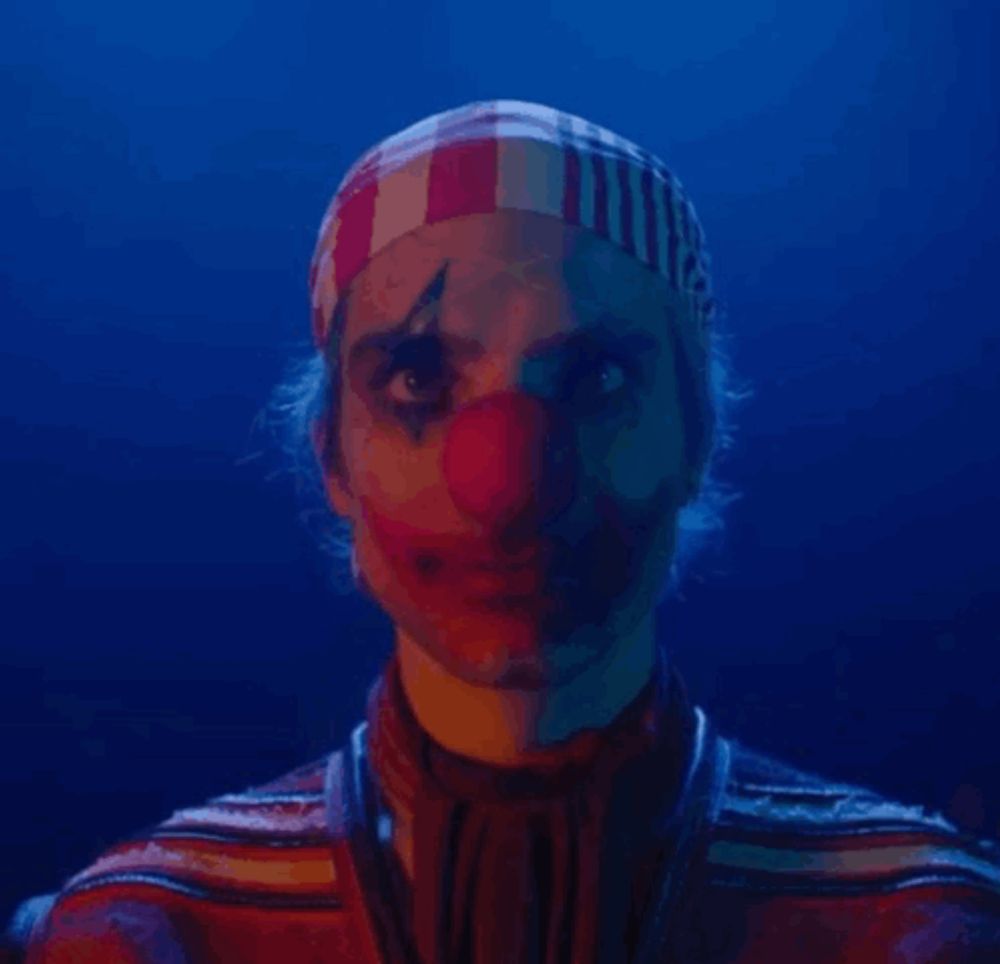 a man dressed as a clown with a red nose and a striped headband on his head .