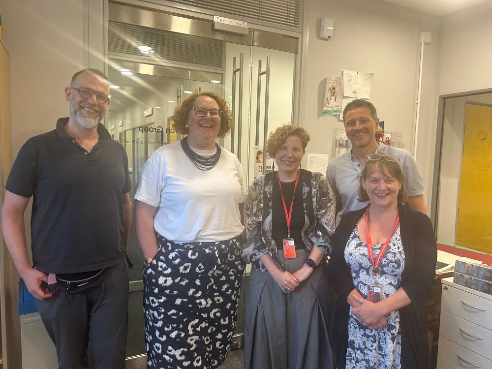 Five people are standing in an office, smiling at the camera. 