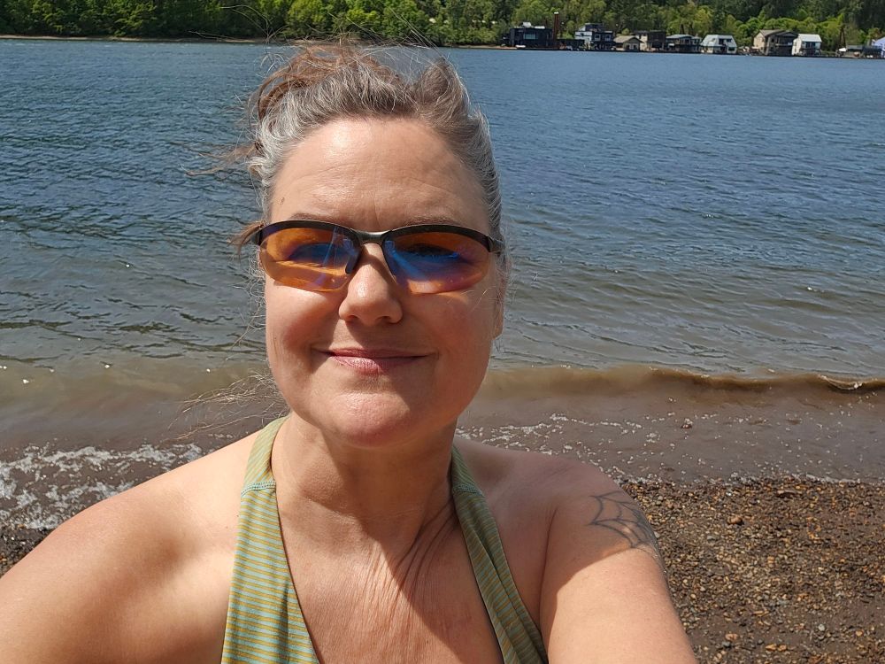 Shoulders up, myself with the river and far bank behind me. I'm smiling no teeth showing bc i think I look better like that and I'm wearing my sport sunglasses in part bc i rode her on my bike and bc there nothing to catch them on my hair when I shove them out of the way and forget they're there until I wonder why my helmet doesn't fit. 