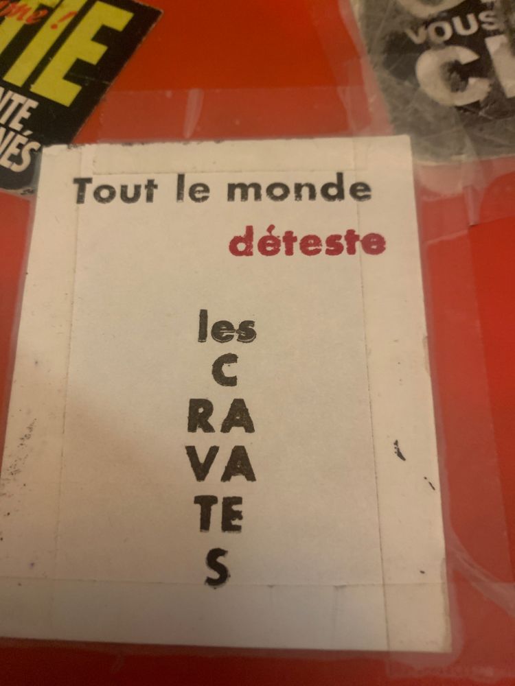 Photo d’un autocollant un peu à l’arrache sur papier ordinaire, mais imprimé en typo plomb à l’ancienne. 

Le te texte dit « Tout le monde déteste / les cravates », le mot déteste est en rouge, et « les cravates » est composé en forme ben de cravate