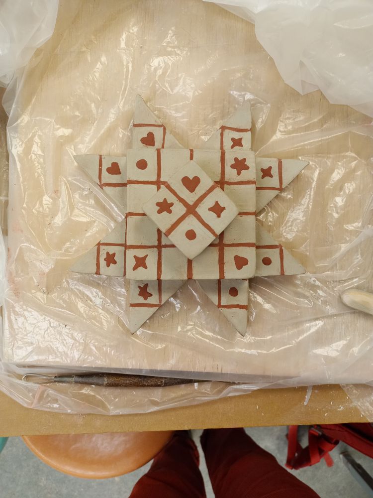 Photo of the same ceramics piece while still in progress. The grid design on the surface is made with slip and features star, heart, circle, and diamond symbols.