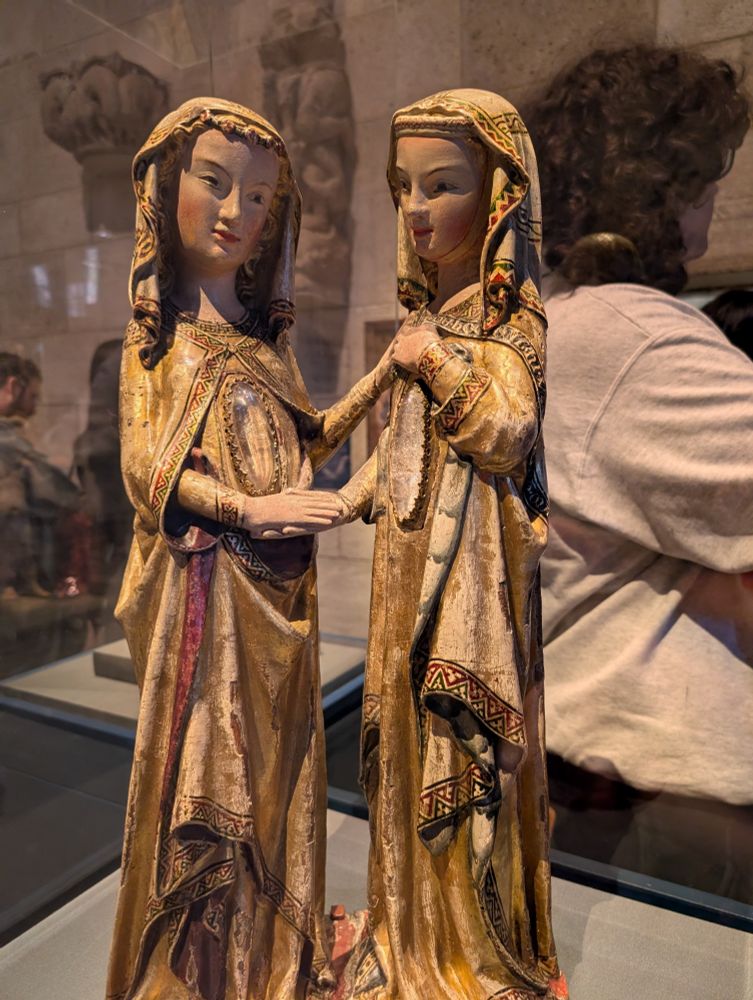 Sculpture of two women holding hands. Each one has a very large and transparent crystal on the front of their chest that is the length of their torsos 