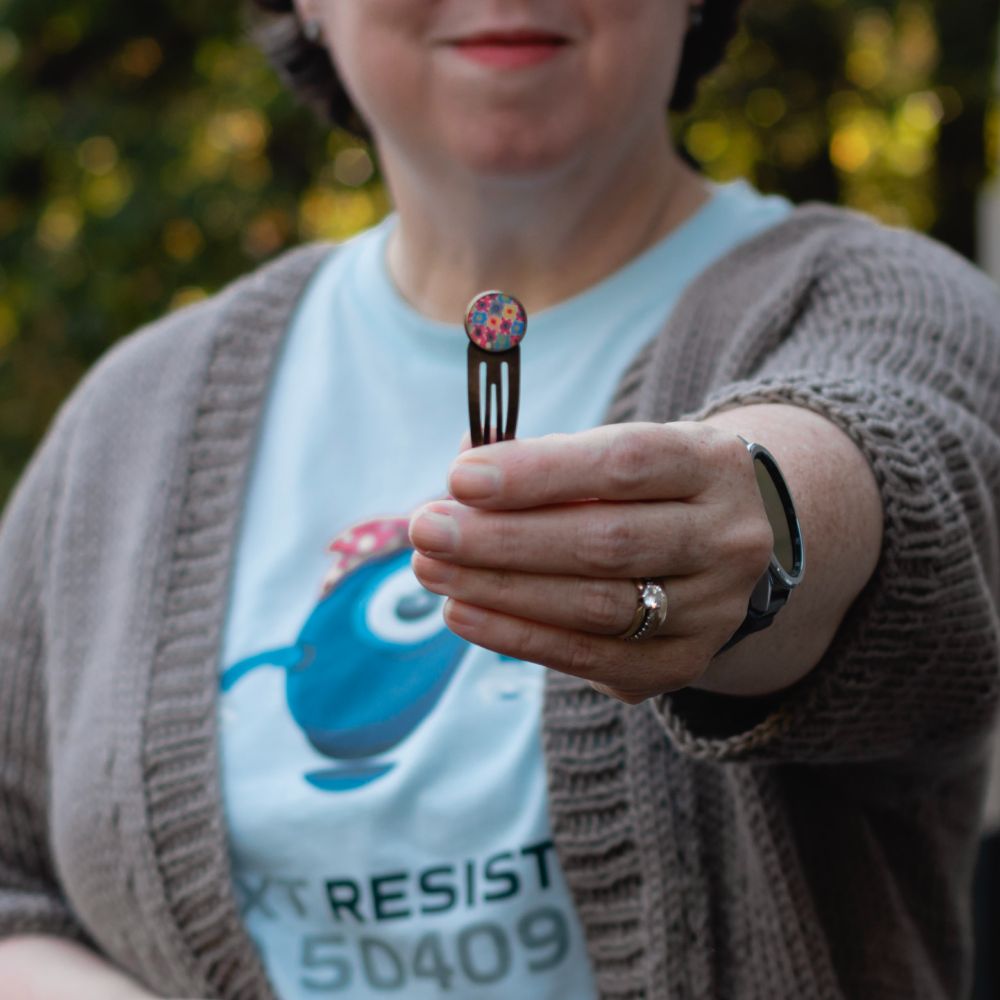 Me, holding a bronze-colored snap hair clip with a bezel on the end, which I have filled with one of my polymer clay designs. I think they're fun with my newly short hair. What do you think? Should I make more of these? Are they good matte? Or should I put a blob of resin on top to make them domed and shiny?