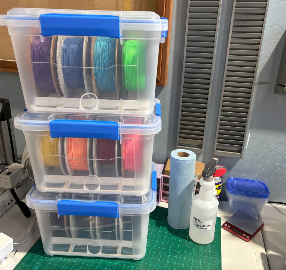 Three waterproof containers full of 3d printing filament spools stacked on top of a desk.