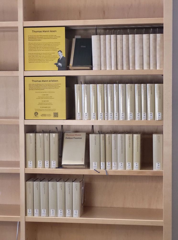 Blick auf das Themenregal "Thomas Mann" in der Leselounge der Herzogin Anna Amalia Bibliothek. 4 gefüllte Bücherregale und zwei gelbfarbene Infotafeln mit Informationen zu Thomas Mann mit den Überschriften "Thomas Mann lesen" und "Thomas Mann erleben"