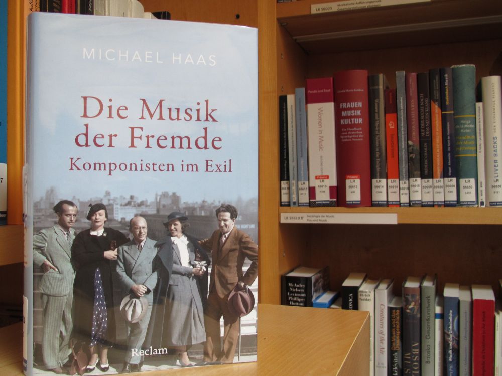 Wiedergegeben ist das Cover des empfohlenen Buches „Die Musik der Fremde: Komponisten im Exil“ von Michael Haas, welches eine Photographie einer Gruppe der im Band beschriebenen Musiker:innen offeriert.