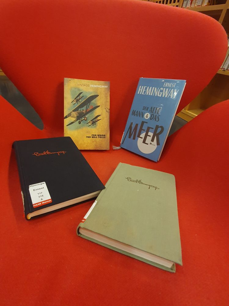 Auf einem roten Lesesessel sind vier Bücher des Schrifstellers Ernest Hemingway platziert. 