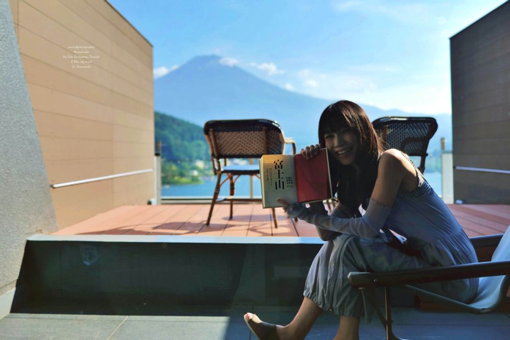 富士山を背景に富士山の本を見せる女性