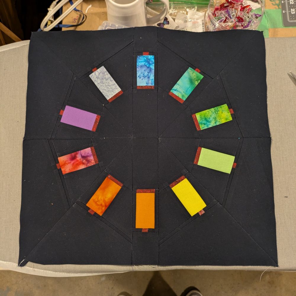 finished quilt block: a circle of rainbow thread spools on a black background