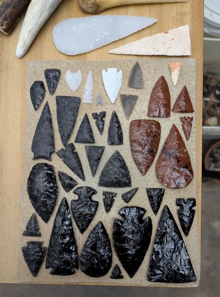 Photo of various types of flintknapped points on a leather pad. Black Obisidan, Dacite, Mahogany Obsidian, Novaculite, Georgetown, and Keokuk materials. 
