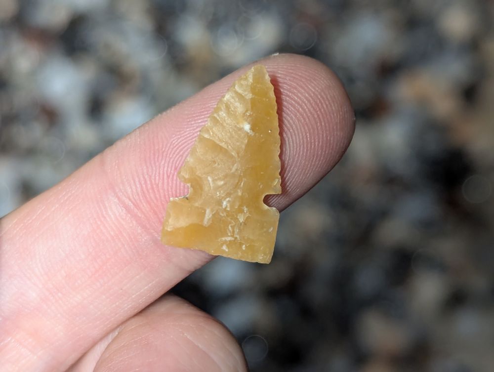 Small notched flintknapped point balanced on a finger.