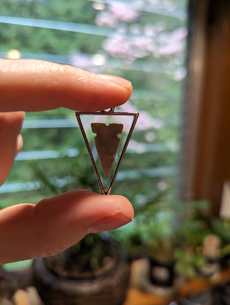 Small tri-notch point made of Burlington Chert in resin in a silver colored triangular pendant.