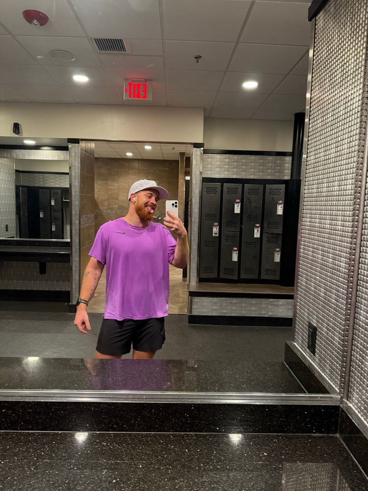 A ginger man sticks out his tongue and takes a selfie in front of the gym bathroom mirror.