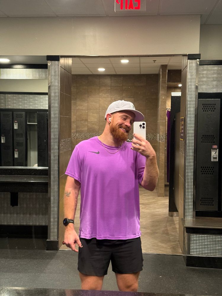 A redhead man smiles in yet another selfie in front of the gym bathroom mirror.