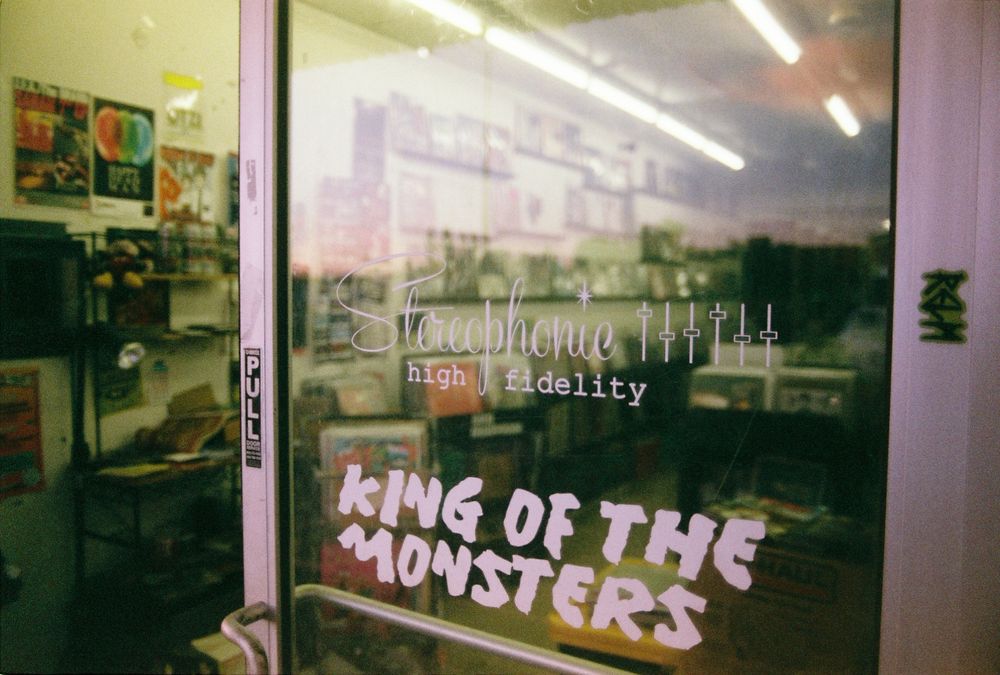 A partially open door to a record store. The door says Stereophone high fidelity with level knob graphics. Below that it says king of the monsters in a stylized font. 