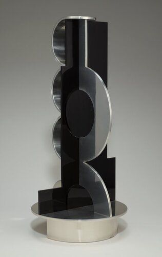 upright sculpture with flat, black, central Plexiglas core with irregularly stepped edges; on one side are three stacked, wide half-circles in polished aluminum; other has one large, flat, polished aluminum arc with another half-arch below touching base; attached to a round polished aluminum base with a foot ring on half of base and a vertical support from center to outer edge under other half of base; shiny black and silver