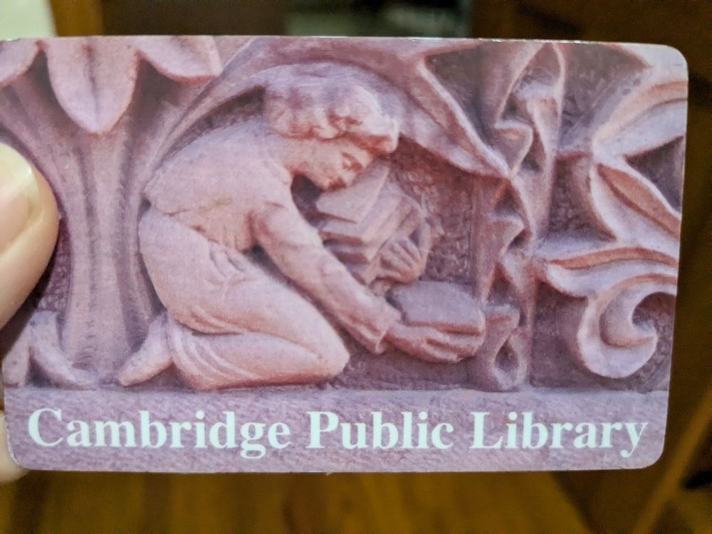Image of a Cambridge Public Library card featuring a photo of a stone carving of a person picking up books, taken from the building facade